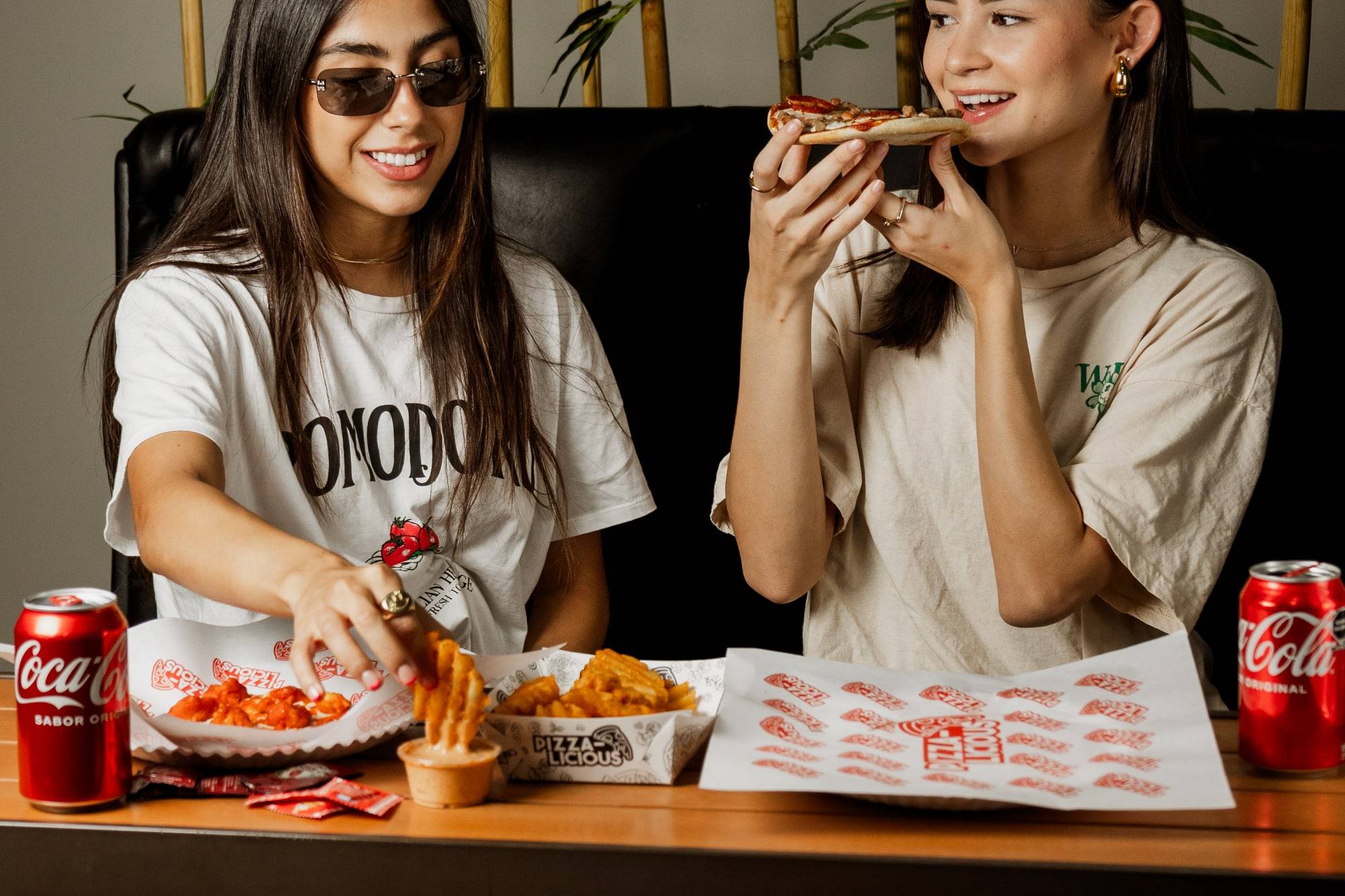 Dos amigas comiendo rebanadas de pizza en Pizzalicious, riéndose