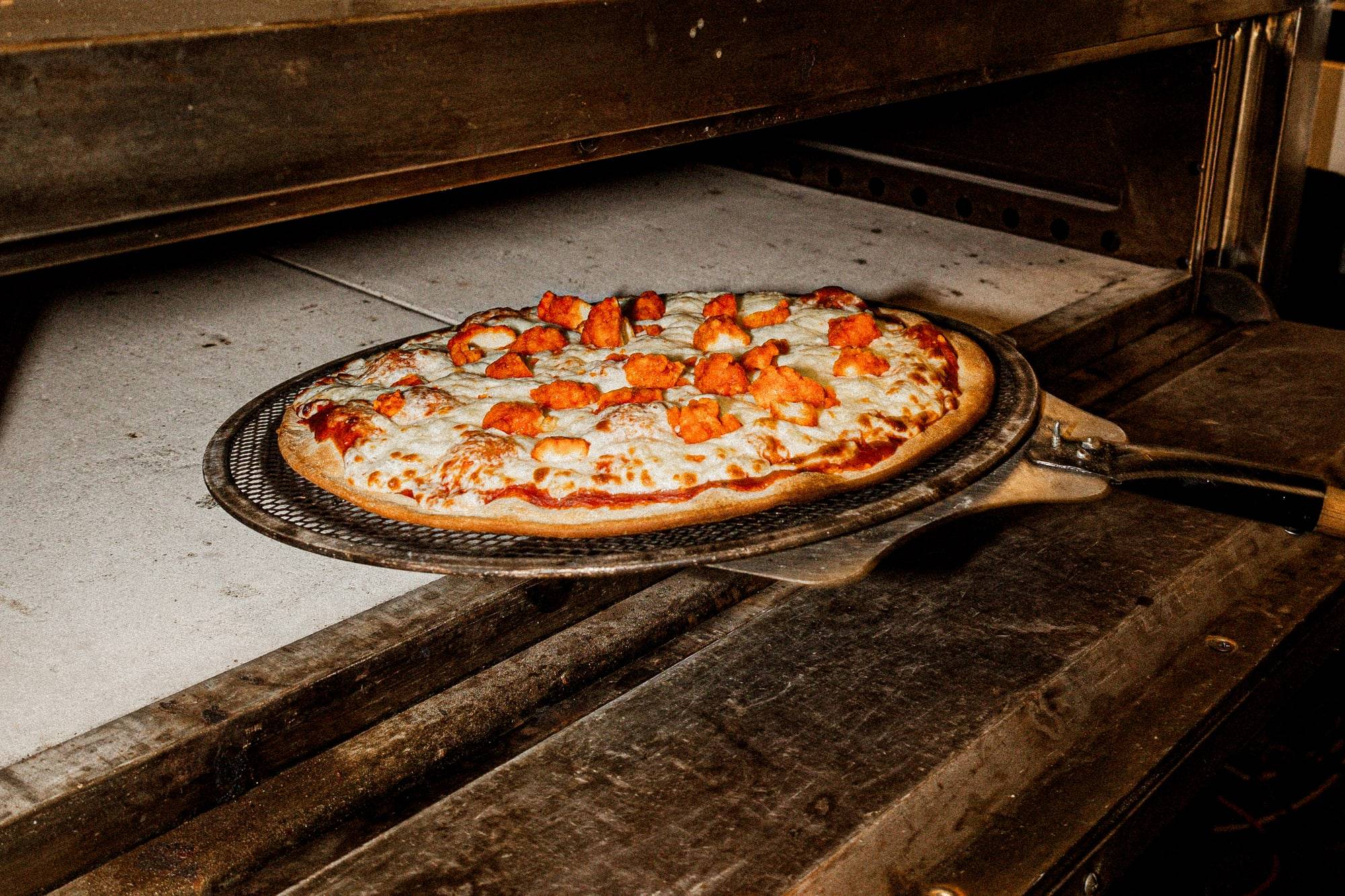 Pizza recién horneada de Pizzalicious sobre la pala de metal, junto a la boca del horno