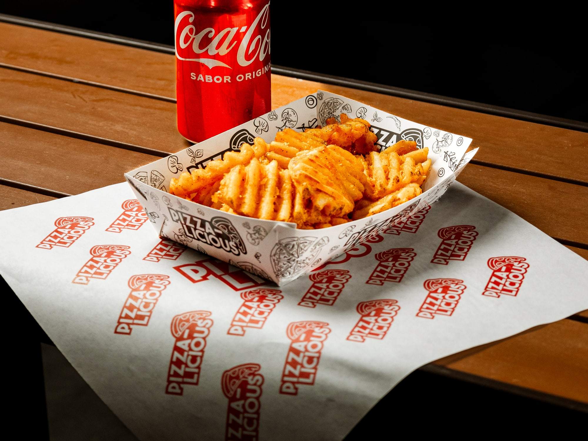 Canasta de papas crisscut de Pizzalicious sobre papel de la casa, junto a un refresco