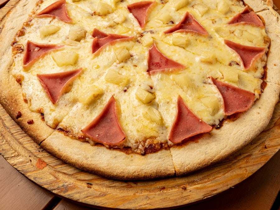Pizza hawaiana de Pizzalicious con jamón y piña sobre tabla de madera, vista desde arriba