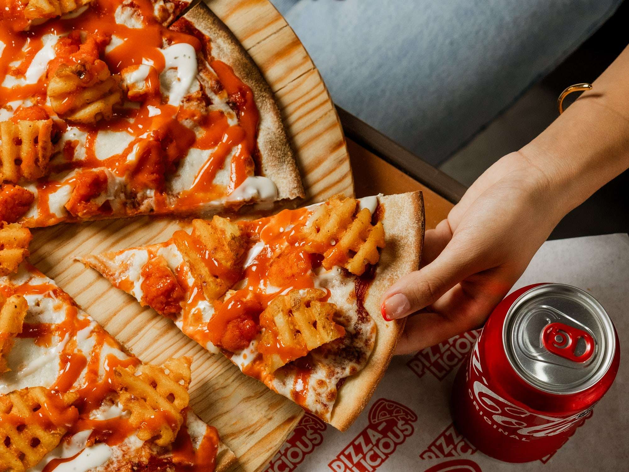 Pizza Monchosa de Pizzalicious con boneless, papas crisscut, salsa búfalo y ranch, con una mano levantando una rebanada