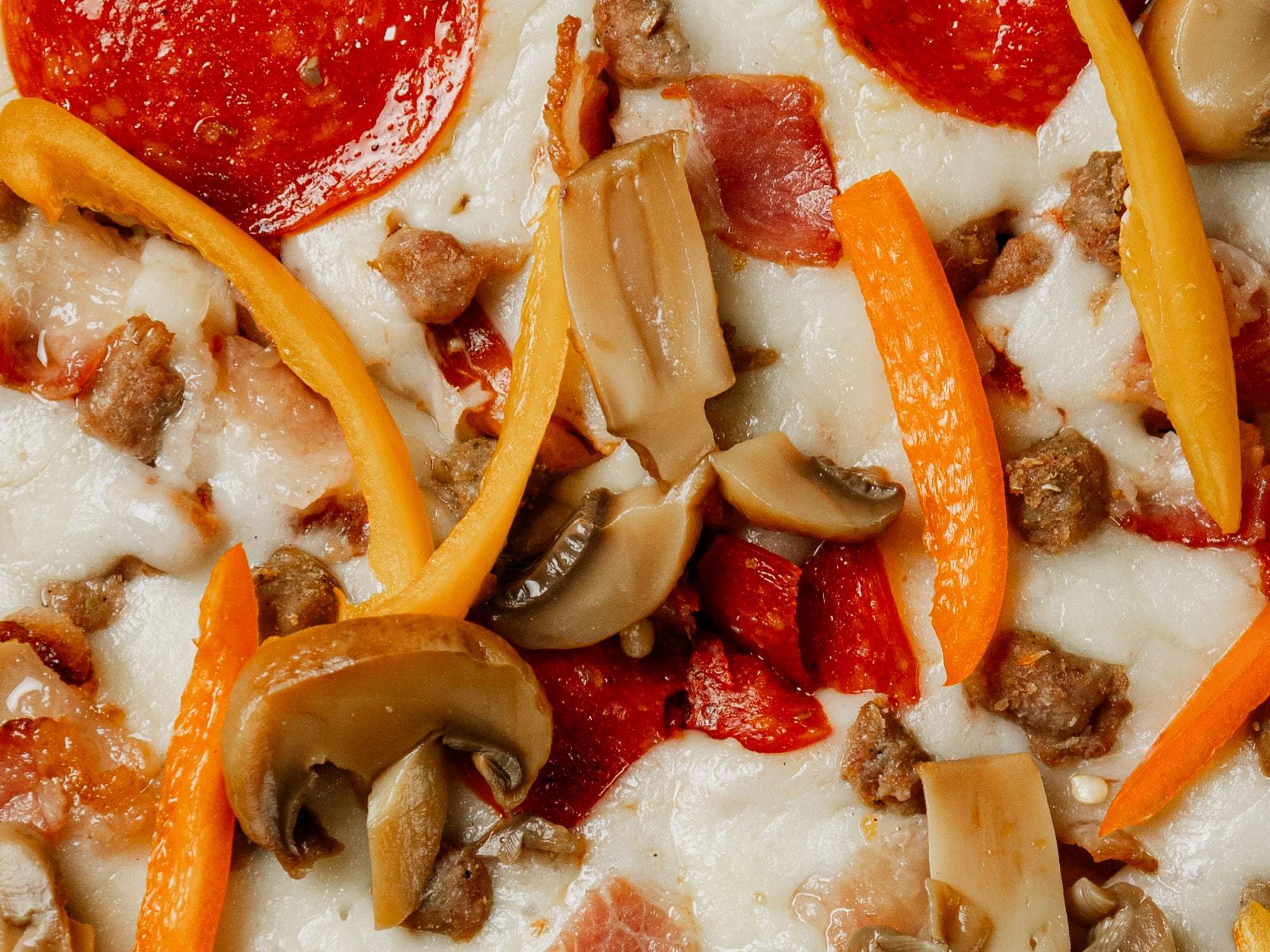 Acercamiento a la pizza Suprema de Pizzalicious con pepperoni, salchicha, tocino, pimiento y champiñón