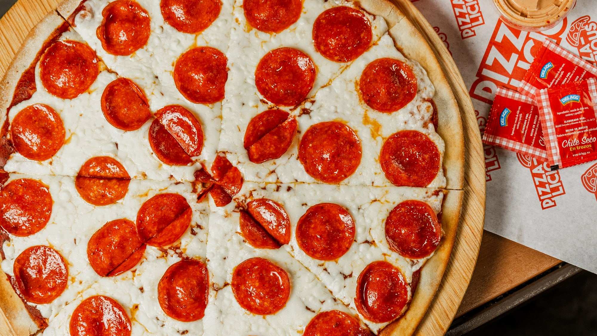 Pizza pepperoni grande de Pizzalicious sobre tabla de madera, vista desde arriba